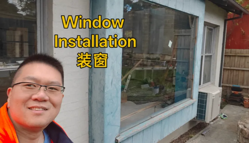 Handyman beside a newly installed large fixed window in a weatherboard wall
