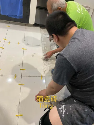 Two workers laying floor tiles with yellow levelling clips between them