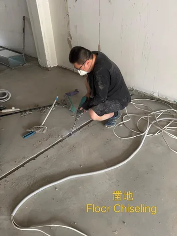 Worker chasing a channel into a concrete floor with conduit laid alongside